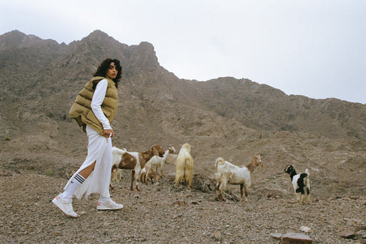 Model walking past goats on a rocky mountainside in white Arwa Al Banawi adidas Forum Low trainers