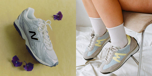 A silver and white New Balance trainer photographed beside purple flowers, next to pale blue and yellow Karhu trainers worn with white socks